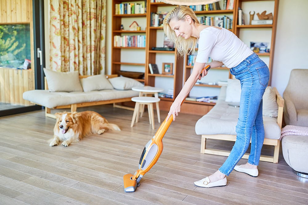 young woman vacuuming the floor near a dog