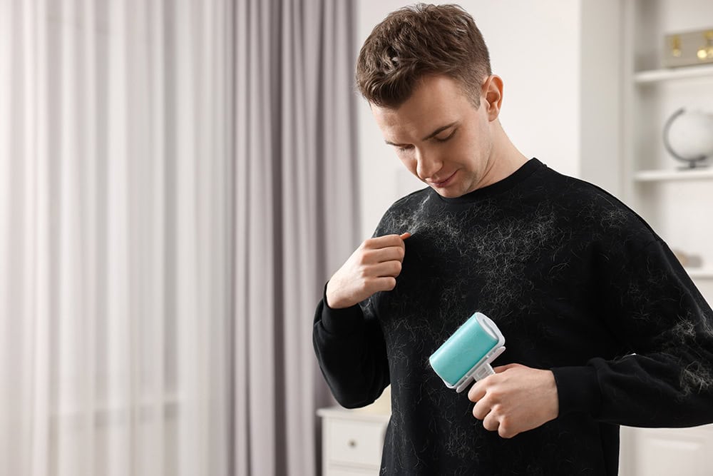 young man using lint roller to remove pet hair in his sweater
