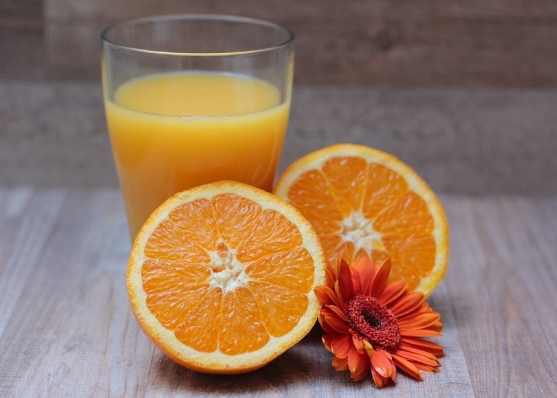 a glass of orange juice behind sliced oranges