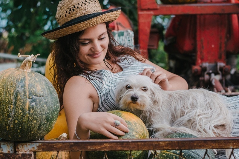 Young countryside woman cuddling her dog while lying among pumpkins_vuk saric_shutterstock
