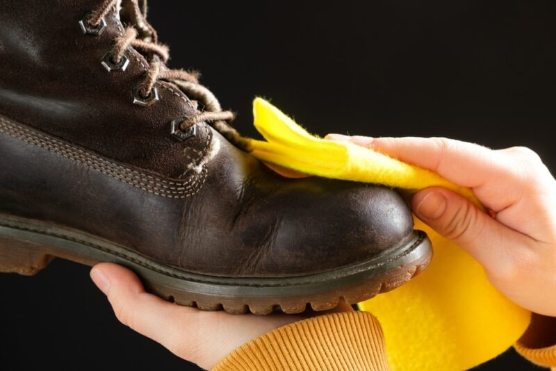 A woman cleans brown nubuck boots on a black background