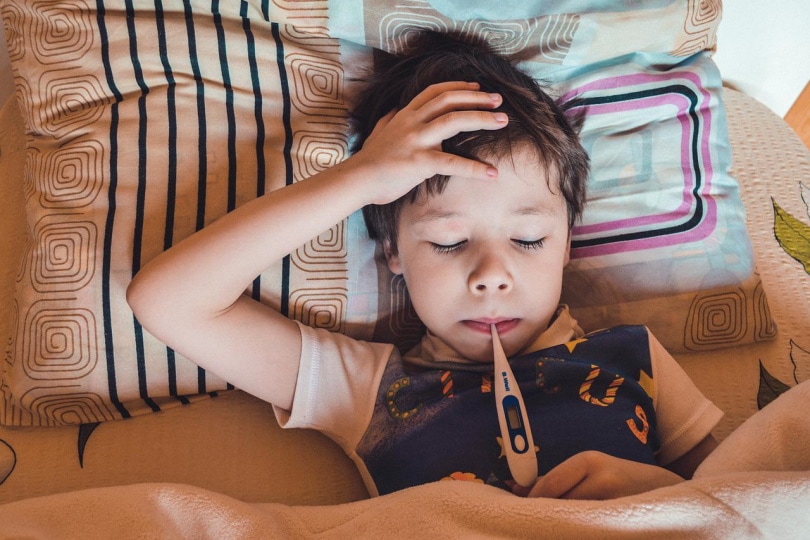 Toddler with oral thermometer in bed