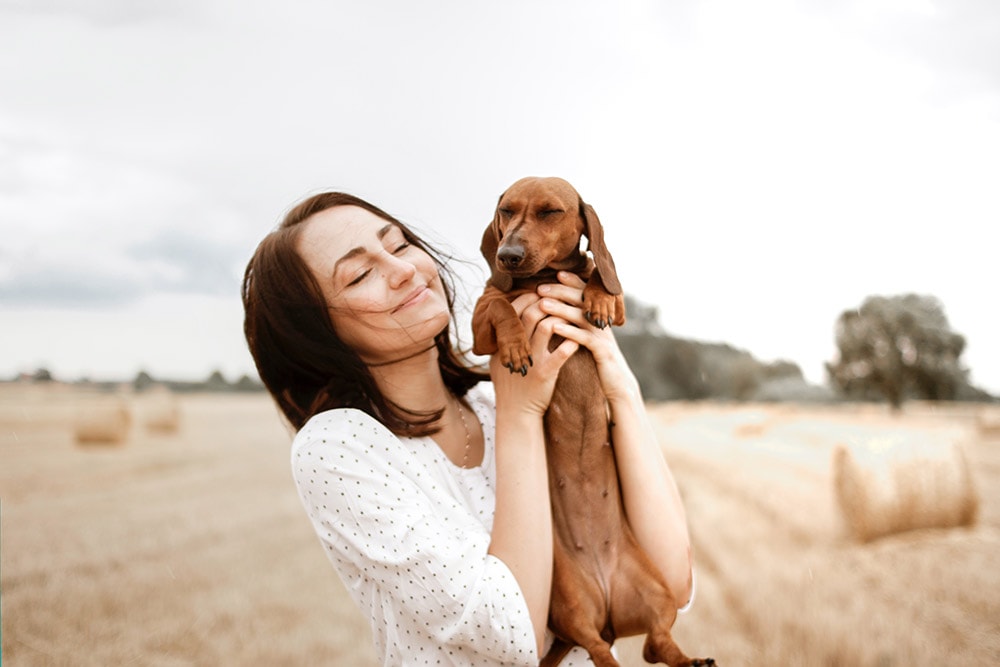 Smiling Woman Carrying Brown Dachshund