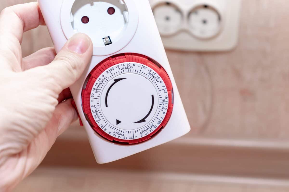 A red and white, dial type mains timer being held in a hand