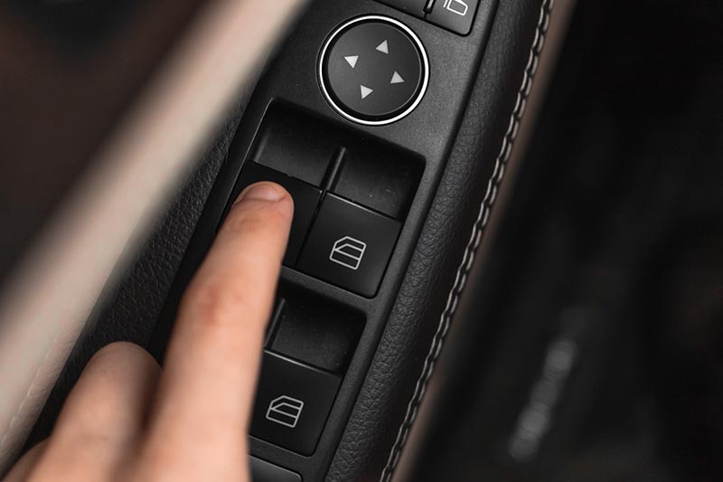 Hand pressing window buttons inside luxury car