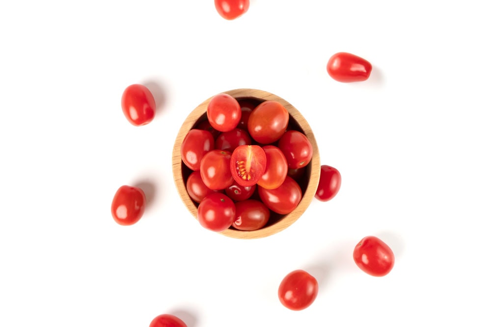 Top view of cherry tomatoes in a wooden bowl isolated on white background