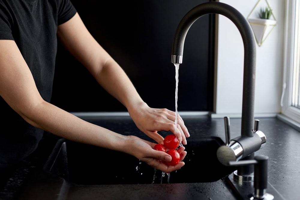Woman shows how to wash a tomato under water in the kitchen with a black background