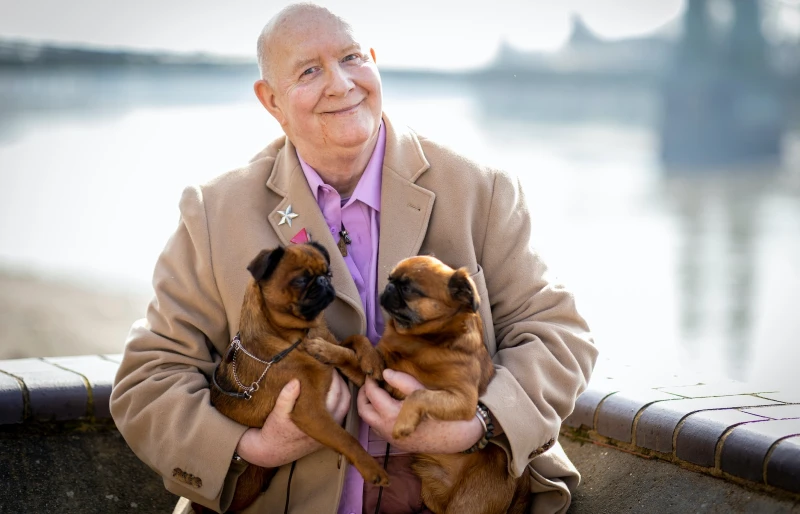 older man holding two apricot pugs in his arms