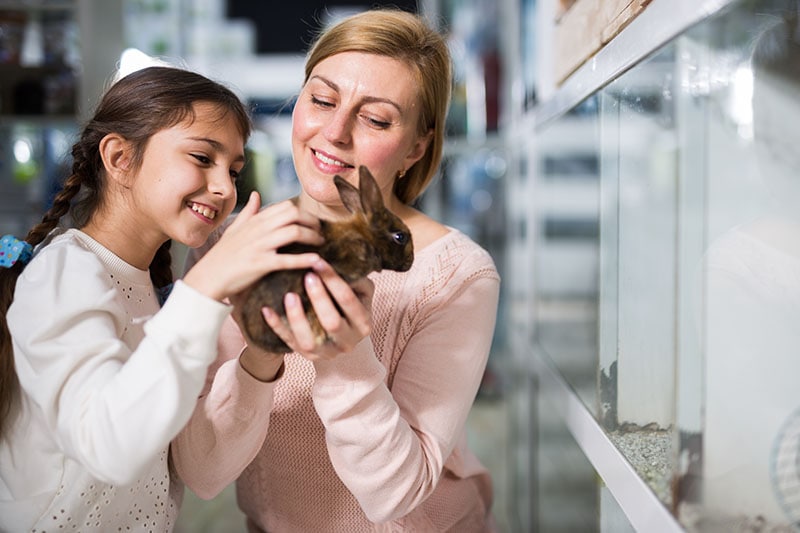 Smiling mother with her happy daughter holding cute rabbit together at pet store