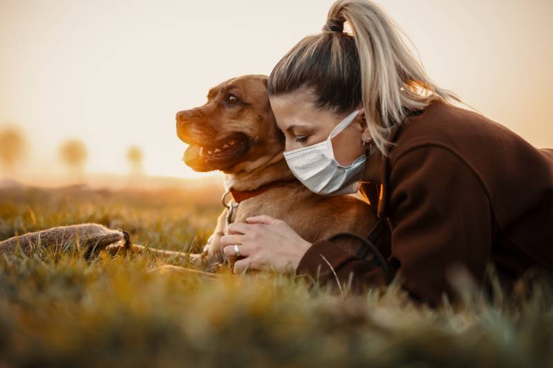 Woman wearing a protective mask is walking alone with a dog outdoors because of the corona virus pandemic