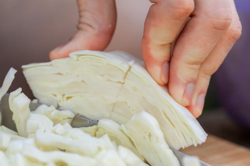 Person cutting fresh cabbage on cutting board