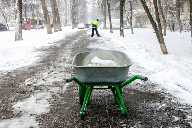 janitor cleans the sidewalk and sprinkles salt