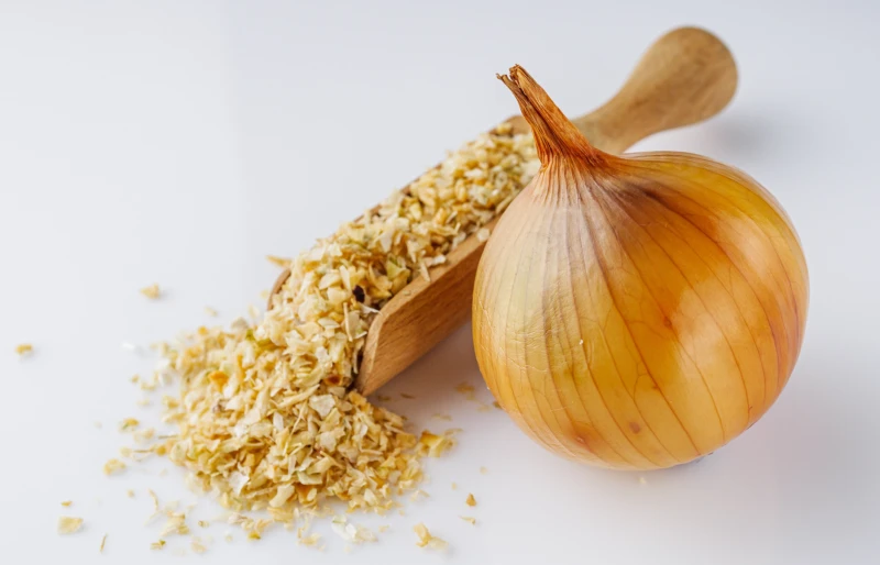 dried onions in wooden scooper with whole onion
