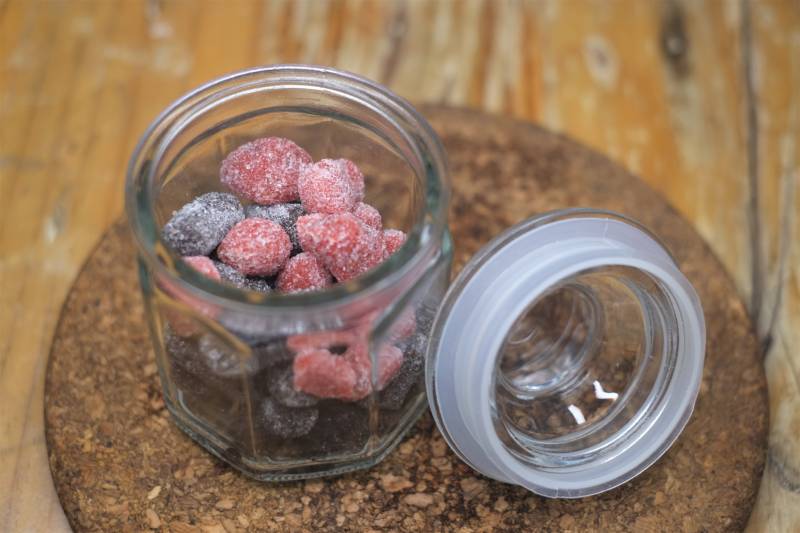 Mixed strawberry and blueberry candy sweets in an open jar on wooden table
