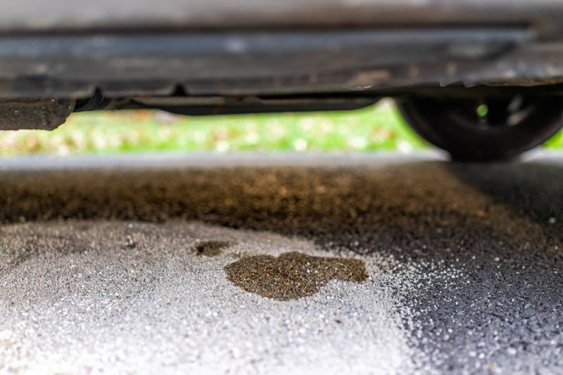 Parked car in driveway with leaking fuel on cat litter to absorb the gas