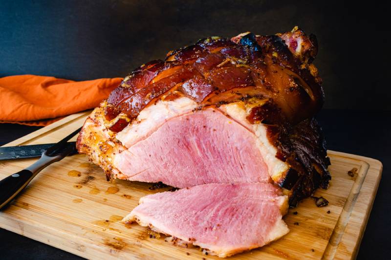 Sliced bone-in glazed ham on a wooden cutting board