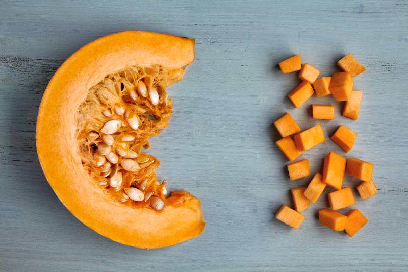 Fresh organic pumpkin slice and diced on a light blue wooden table