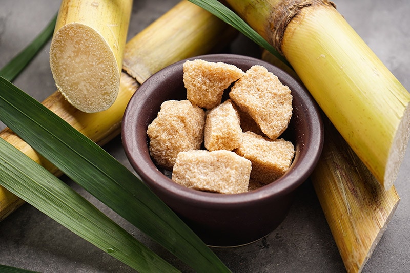 a bowl of granulated sugar surrounded with sugar canes