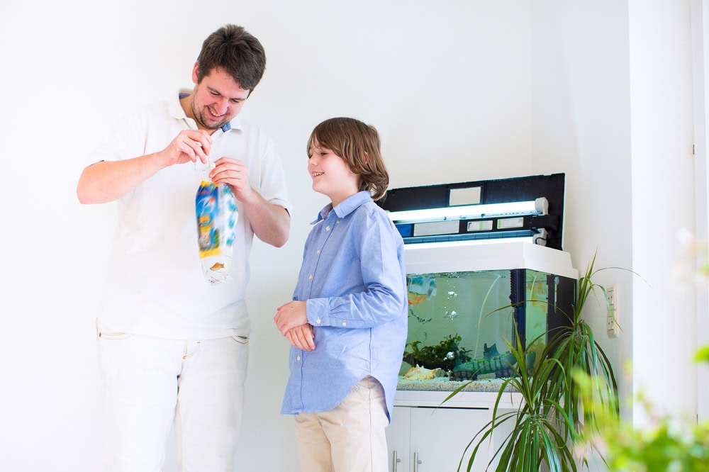 father and son holding a plastic bag with aquarium at the back